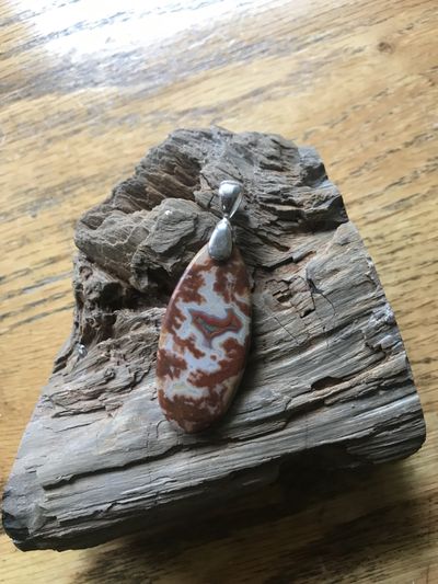 Fairburn agate pendant with red and white banding on a sterling silver bail, resting on driftwood
